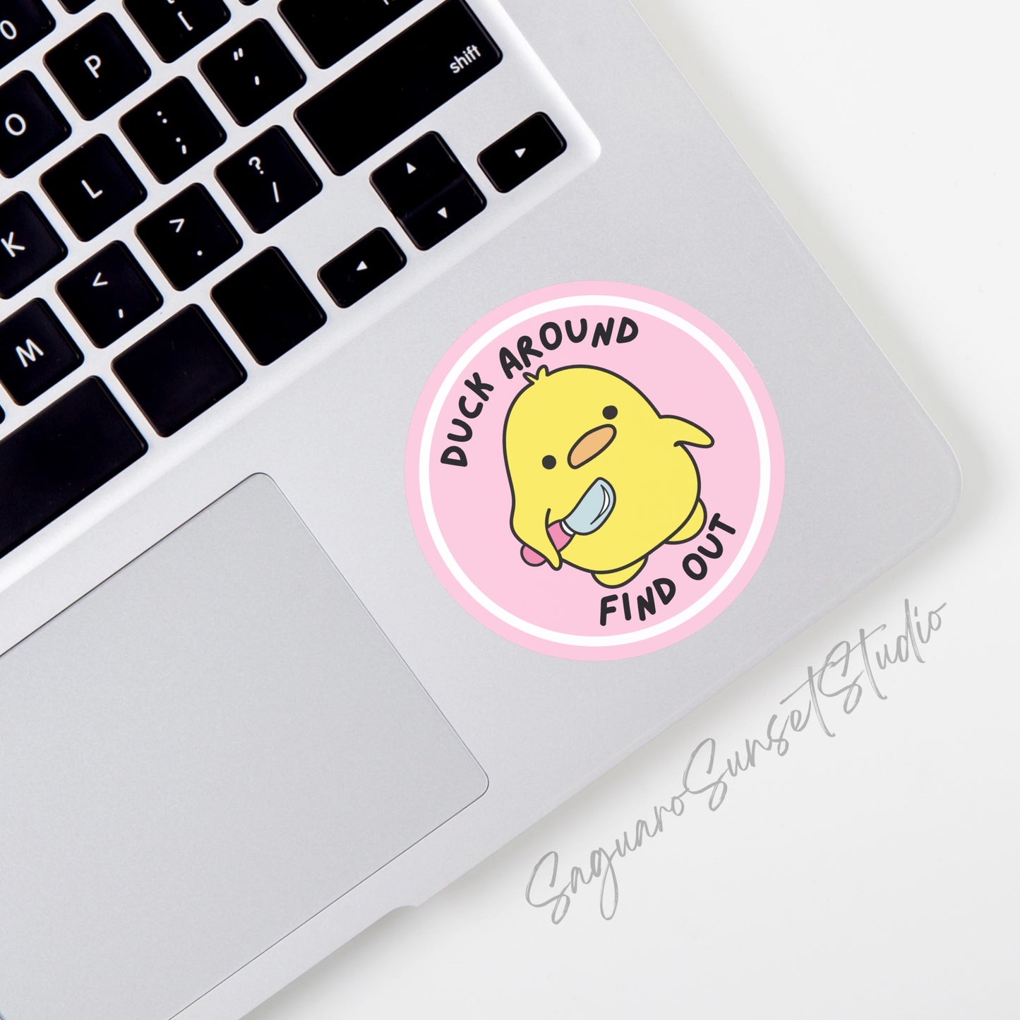 A round vinyl sticker featuring a cute yellow duck holding a small knife, with the phrase "Duck Around Find Out" written in bold black text above and below the duck.