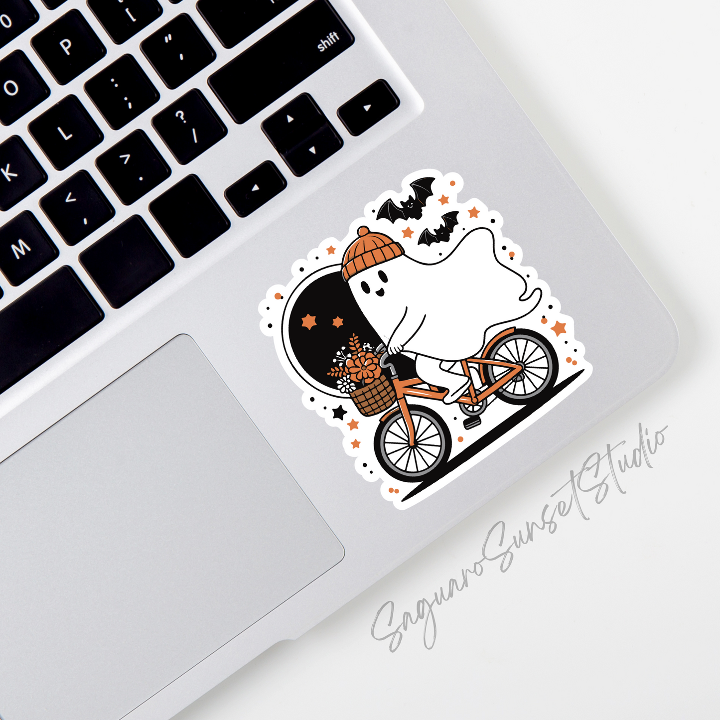 A sticker featuring a cute ghost wearing an orange beanie riding a bike with a basket of flowers, surrounded by bats, stars, and an autumn-themed design.