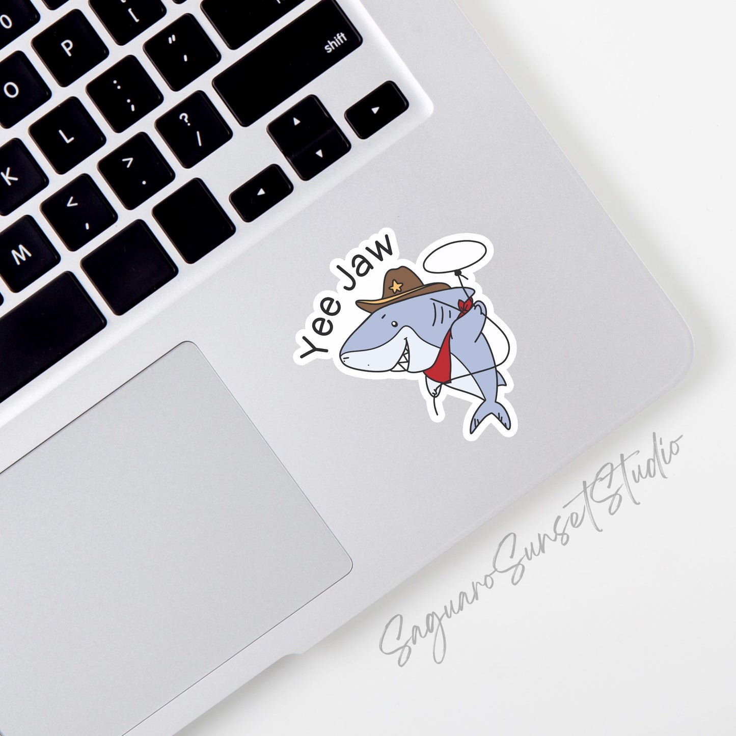 A fun sticker depicting a shark dressed as a cowboy with the phrase "Yee Jaw," perfect for adding humor and personality to any surface.