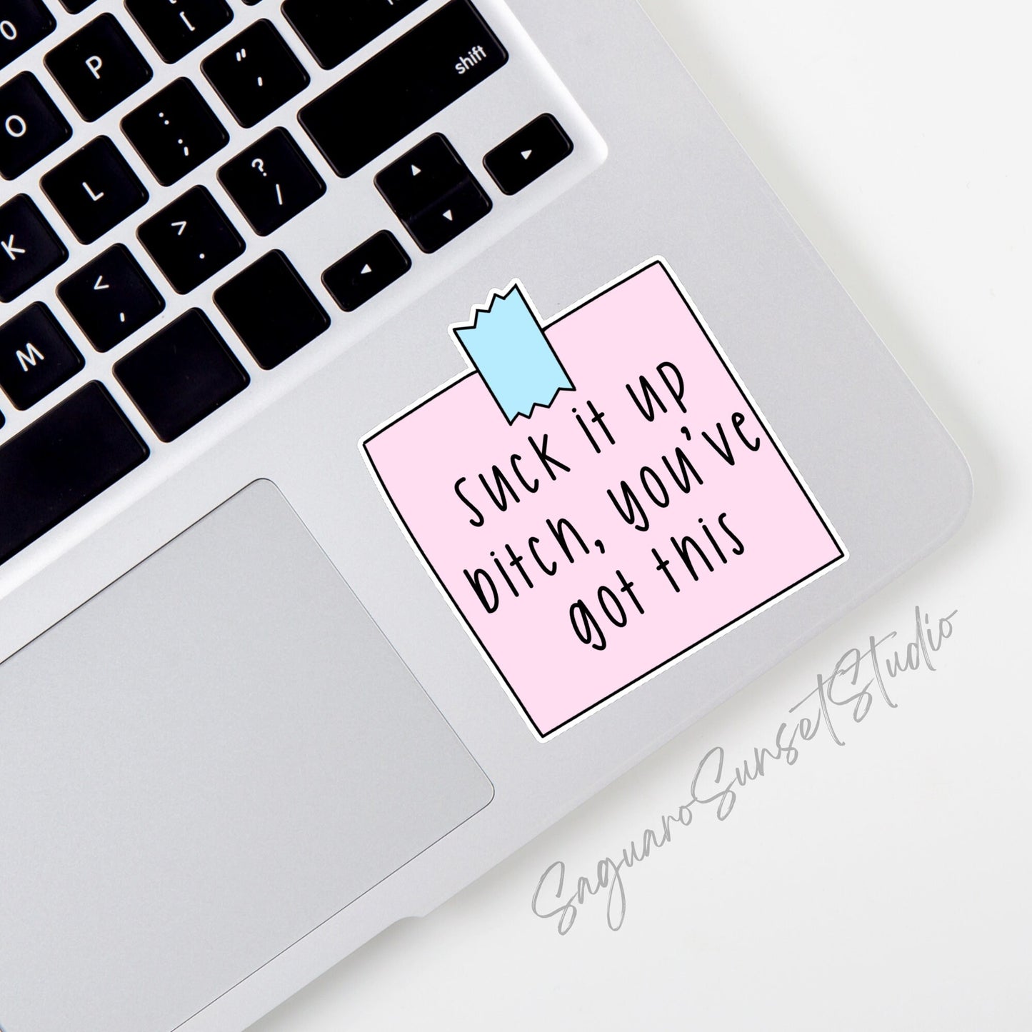 A sticker featuring the phrase "Suck it up bitch, you’ve got this" written in black text on a pink rectangular note. The note is secured with a blue piece of tape at the top.