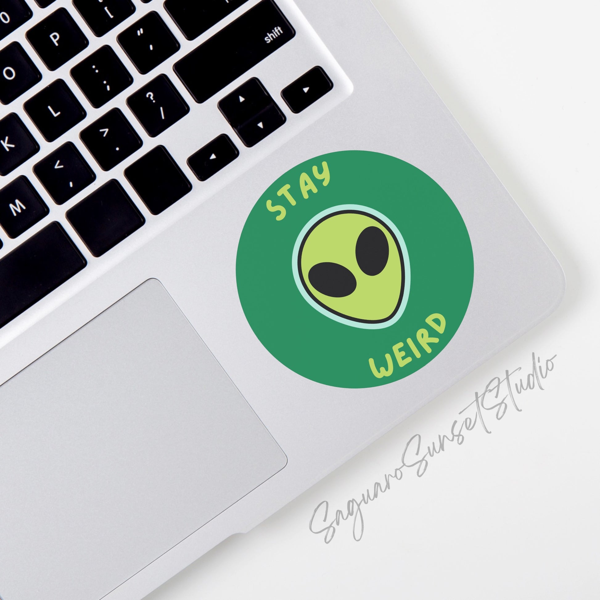 Circular sticker with an alien face and the phrase "Stay Weird," perfect for adding a touch of uniqueness to your belongings.