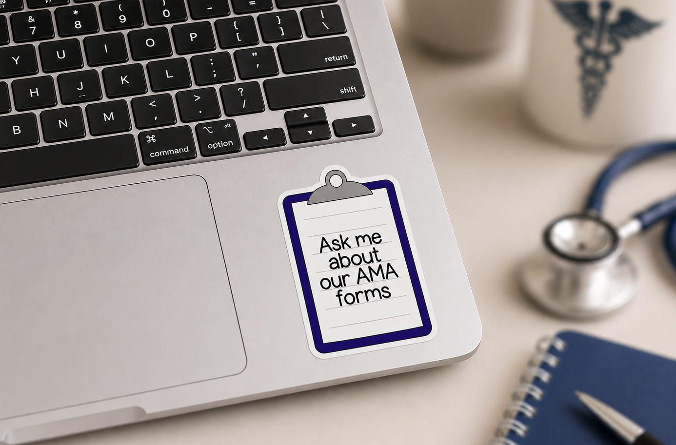 A close-up of a silver laptop with a white sticky note on the palm rest that reads 'Ask me about our AMA forms' in black text, surrounded by a stethoscope, notebook, and mug on a light beige desk.