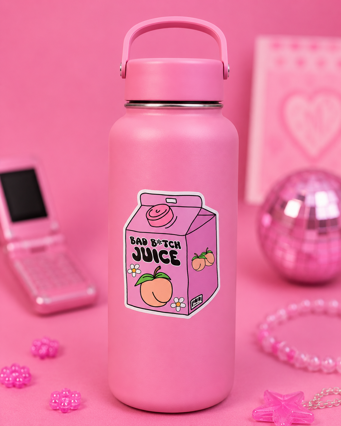 A pink insulated water bottle with a carry handle, featuring a cartoon juice carton sticker that reads 'BAD B*TCH JUICE' with peach illustrations. The bottle is centered on a pink background with decorative pink accessories around it.