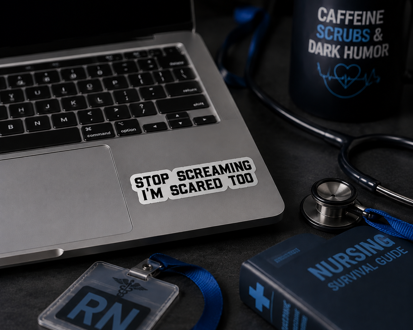 A white rectangular sticker with black text reading 'STOP SCREAMING I'M SCARED TOO' applied to the palm rest of a silver laptop. The scene is styled with medical-themed props, including a stethoscope, a black mug with blue text, a blue 'NURSING SURVIVAL GUIDE' book, and an ID badge holder.