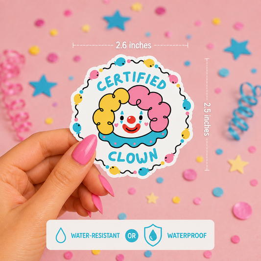 A hand with pink manicured nails holds a die-cut sticker featuring a cartoon clown face with yellow and pink hair, red nose, and blue collar, surrounded by the words 'CERTIFIED CLOWN' in blue. White dashed lines show dimensions of 2.6 inches wide by 2.5 inches tall.