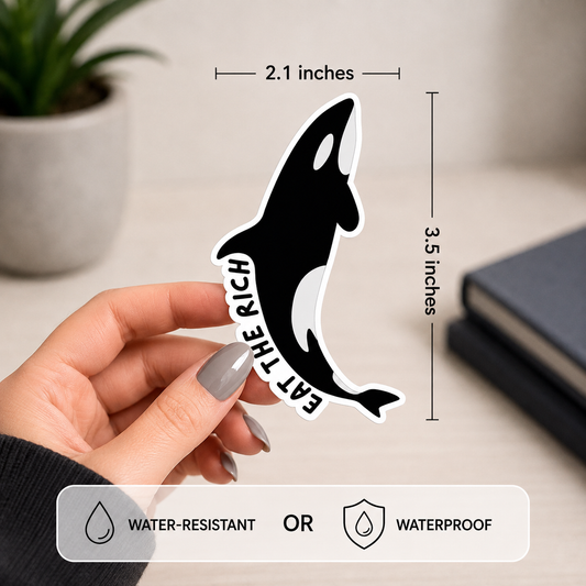 A hand holds a black and white orca-shaped sticker with the text 'EAT THE RICH' written vertically. The image includes dimension labels showing 2.1 inches by 3.5 inches tall