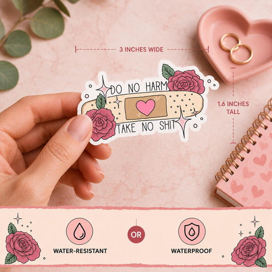 A hand holds a die-cut sticker featuring a pink rose, a beige bandage with a pink heart, and the text 'DO NO HARM TAKE NO SHIT'. The background is a soft pink flat-lay with eucalyptus leaves, a pink heart-shaped dish with gold rings, and a pink notebook.