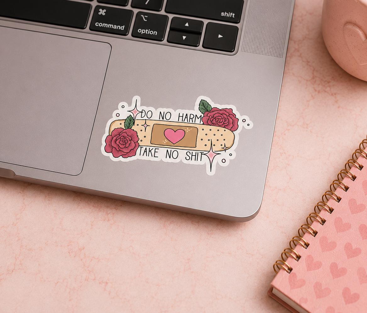 A die-cut vinyl sticker applied to the palm rest of a silver laptop. The sticker features a beige bandage design with a pink heart in the center, flanked by two pink roses with green leaves.