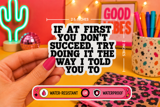 A hand holds a die-cut sticker with the text 'IF AT FIRST YOU DON'T SUCCEED, TRY DOING IT THE WAY I TOLD YOU TO' in bold black letters on a white background. The image includes dimension lines showing the sticker is 2.6 inches wide by 2 inches tall