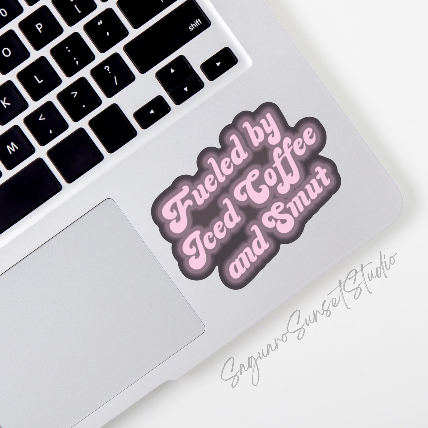 A vinyl sticker with the phrase "Fueled by Iced Coffee and Smut" in playful pink text on a dark background