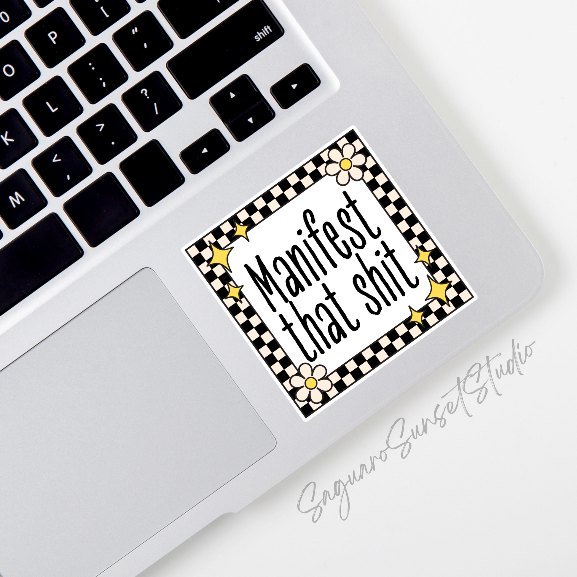 A motivational sticker that says 'manifest that shit' with a black and cream color checkered border with retro star and flower accents.