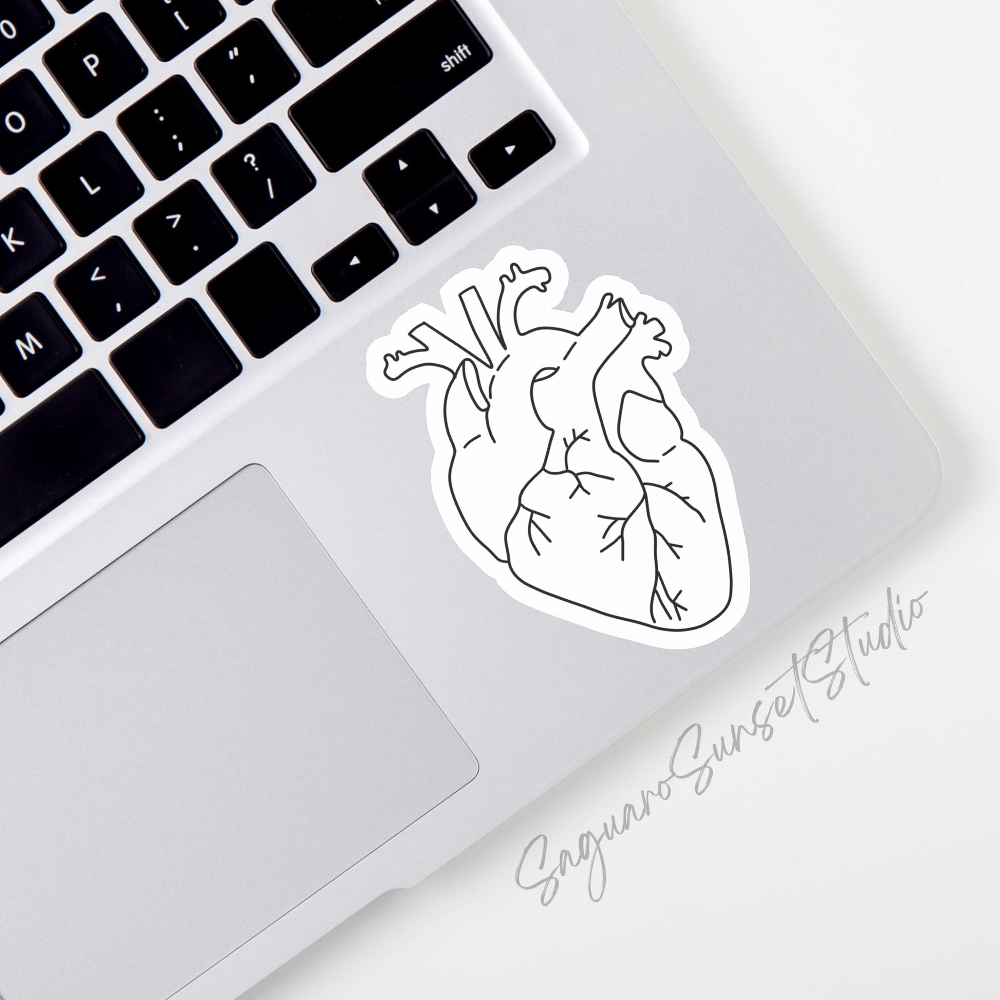 A sticker on the corner of a laptop of a white anatomical heart with black veins.