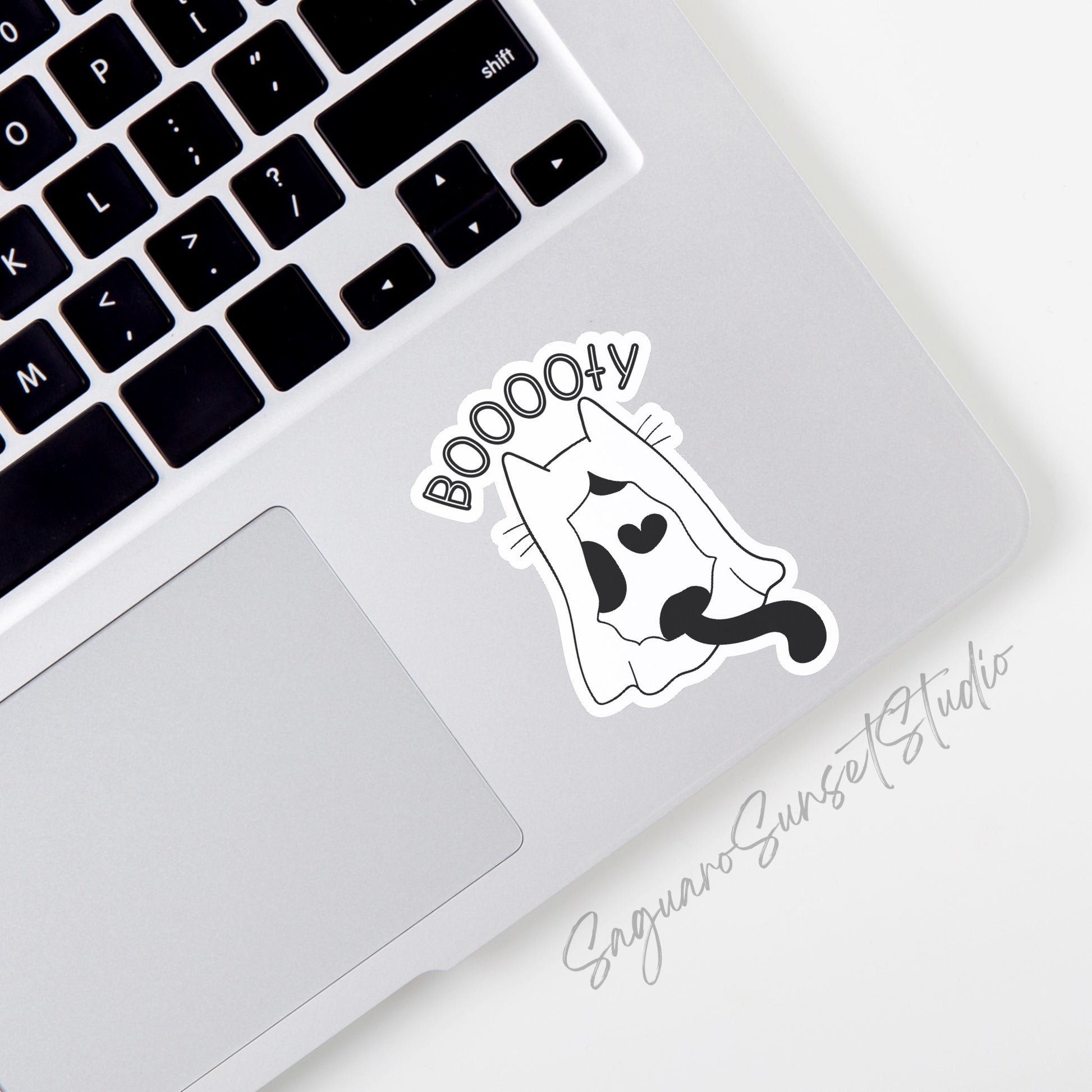 A black and white Halloween sticker featuring a cat ghost with the text 'booooty' placed on the bottom corner of a laptop.