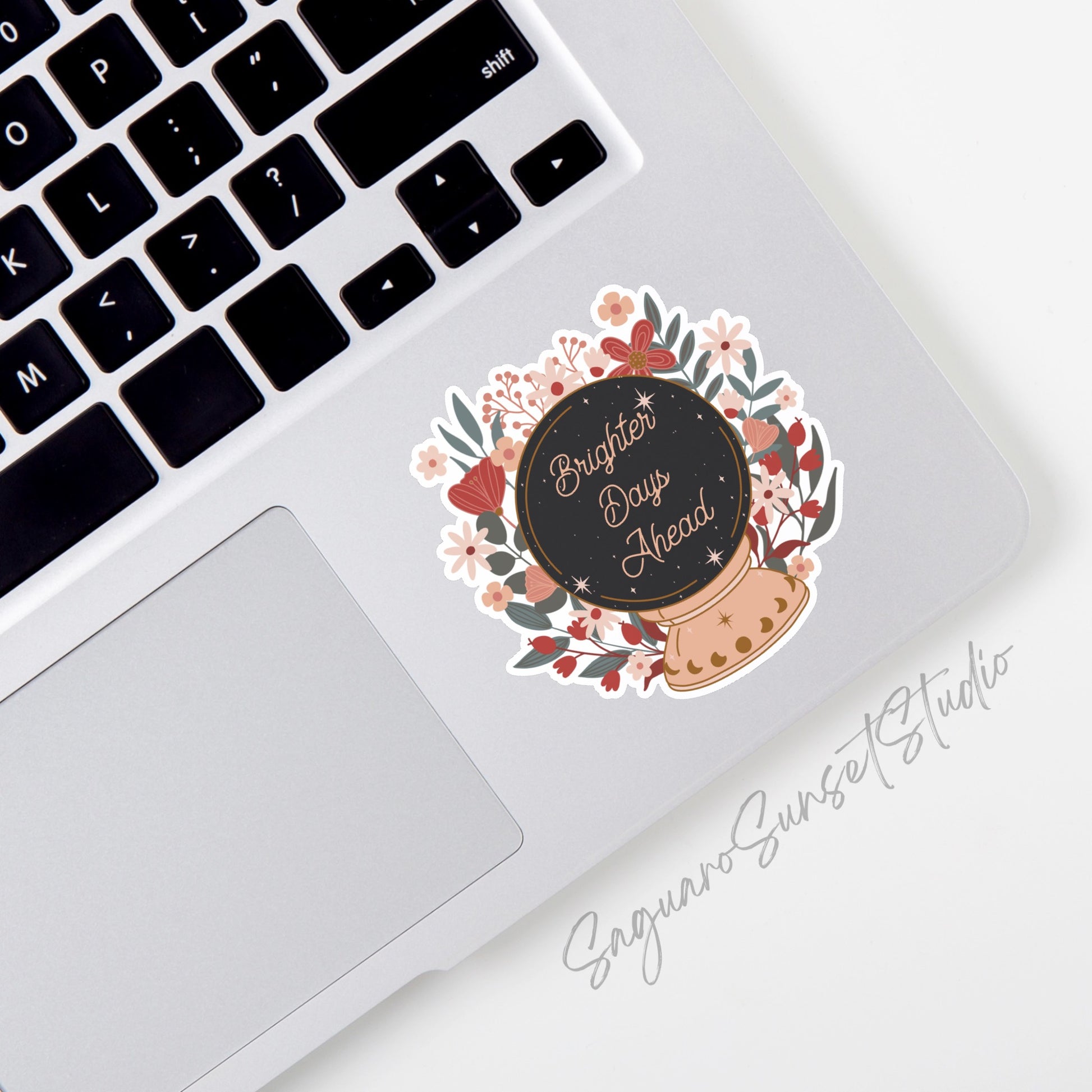 A sticker featuring a floral design surrounding a crystal ball, inside which the text 'Brighter days ahead' on the bottom corner of a laptop.