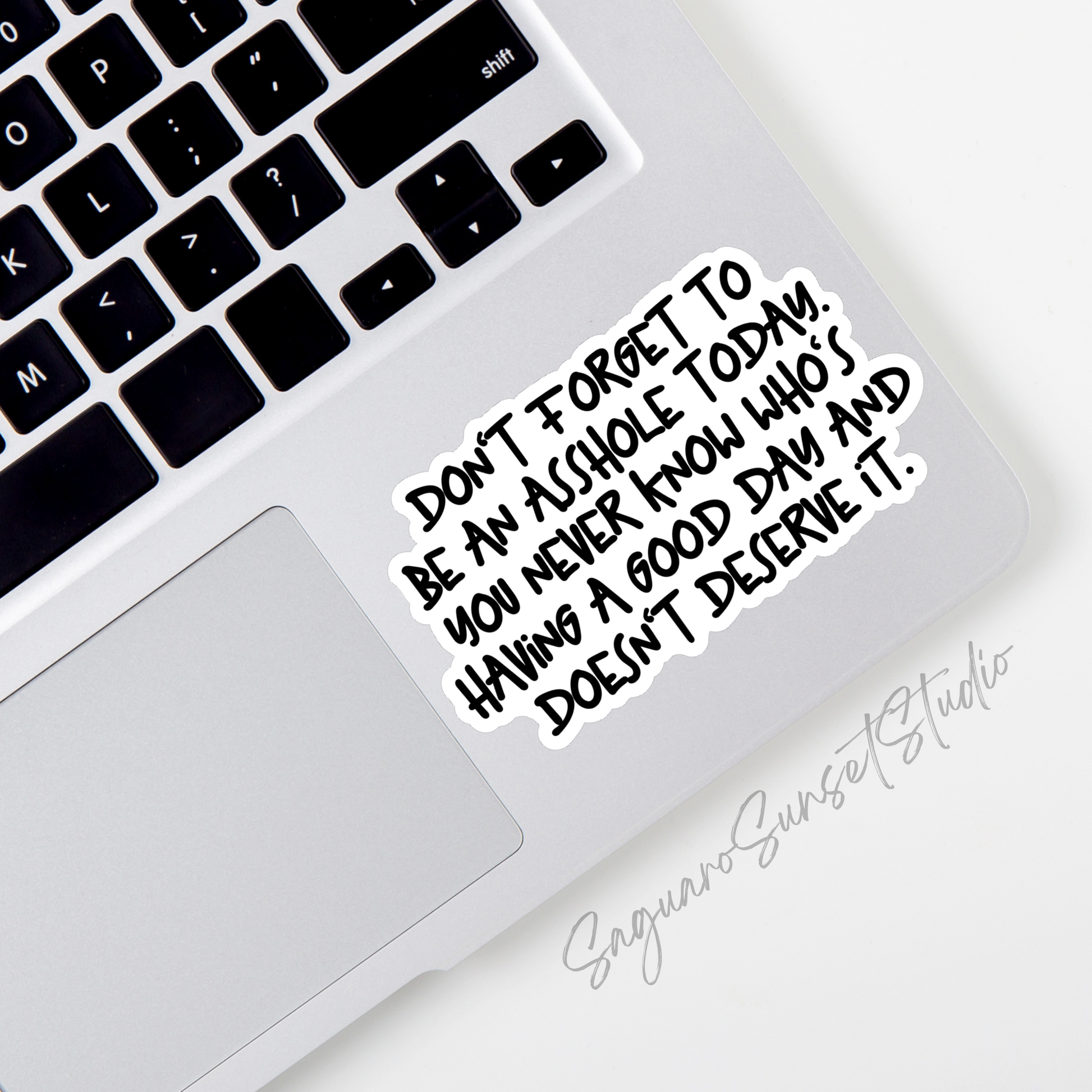 A sticker with black writing that says 'Don't forget to be an asshole today. You never know who's having a good day and doesn't deserve it.'. The sticker is placed on the bottom corner of a laptop.