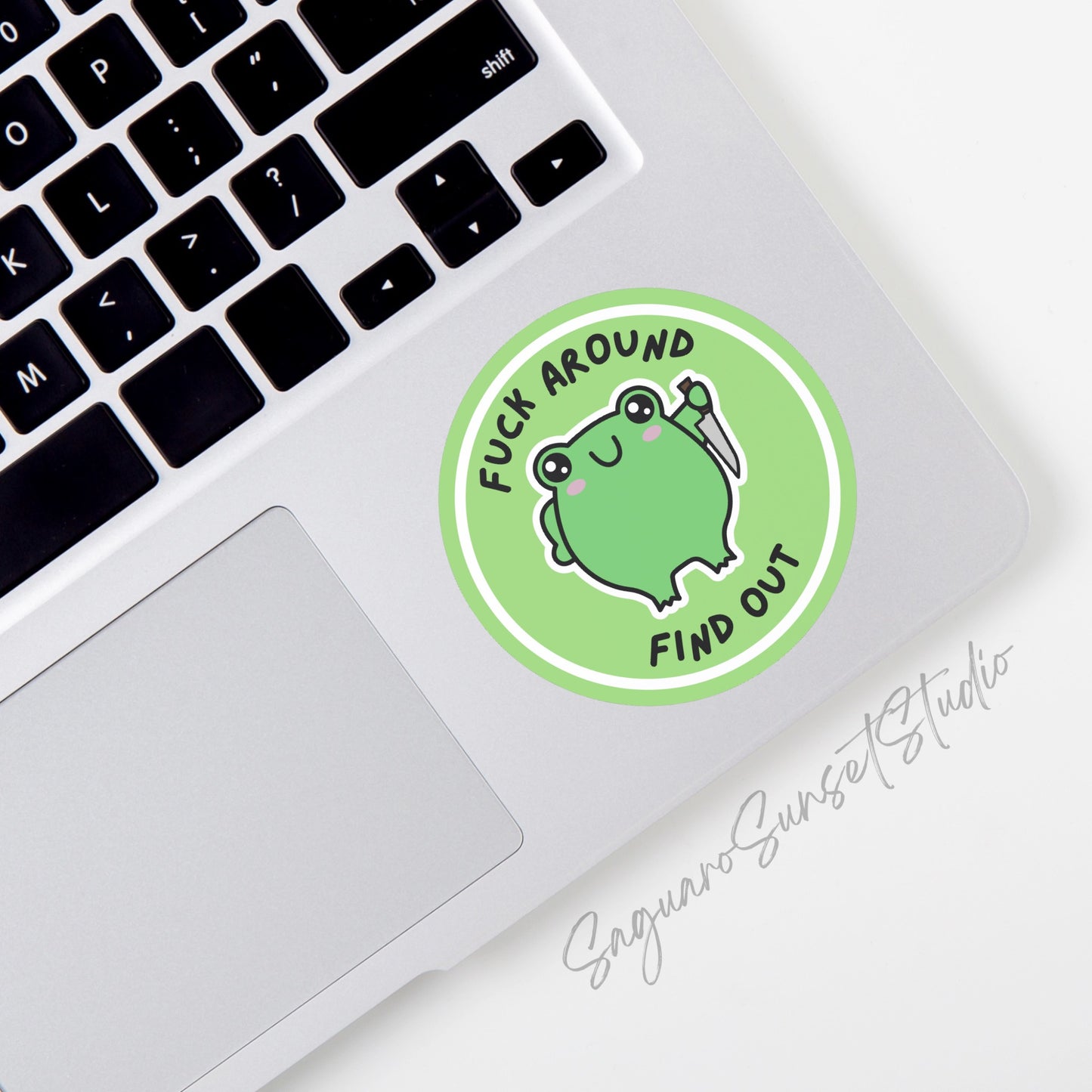 A round vinyl sticker featuring a cute green frog holding a knife, with the phrase "Fuck Around Find Out" in bold black text