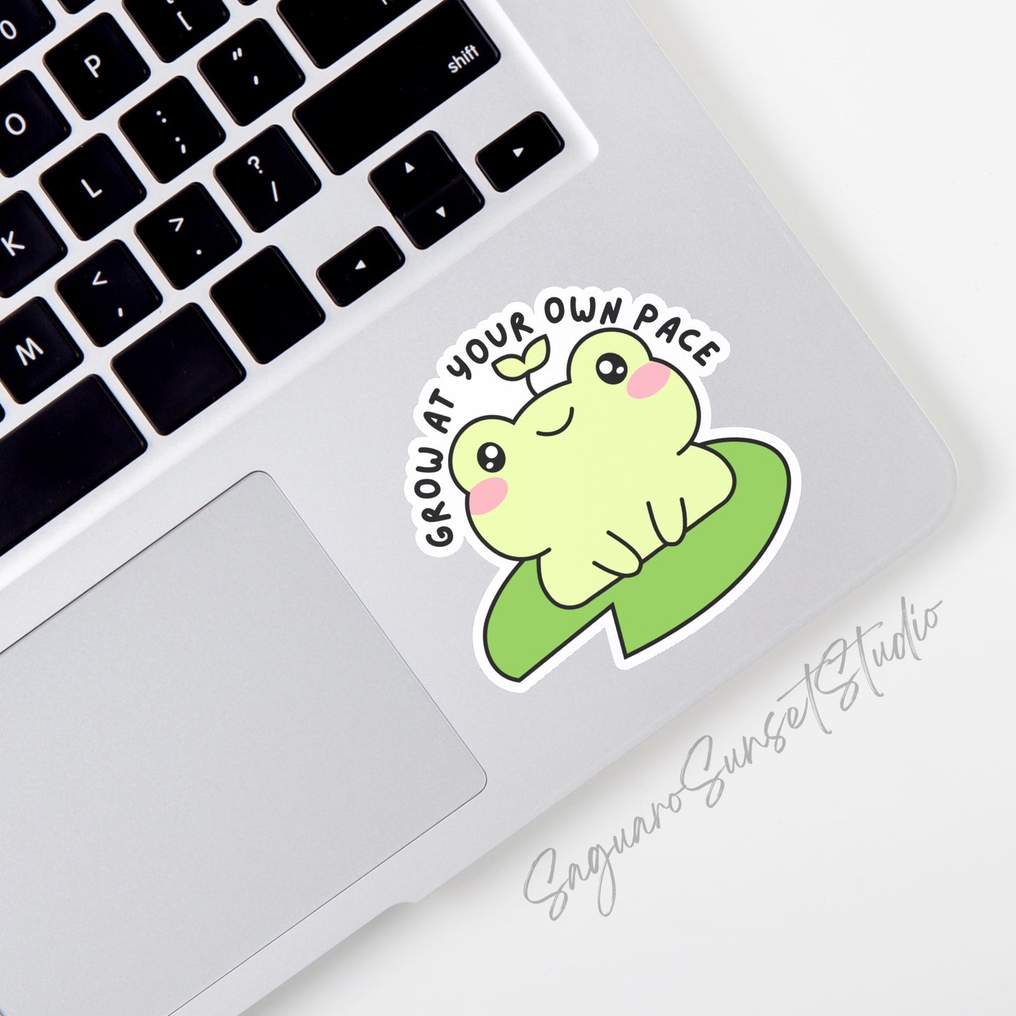 A vinyl sticker featuring a cute frog with a sprout on its head sitting on a lily pad, with the phrase "Grow at Your Own Pace" written above