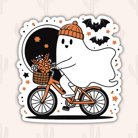 A ghost wearing an orange beanie rides a bicycle with a basket of flowers. Bats fly in the background, with a dark sky and orange stars. The design has a Halloween theme.