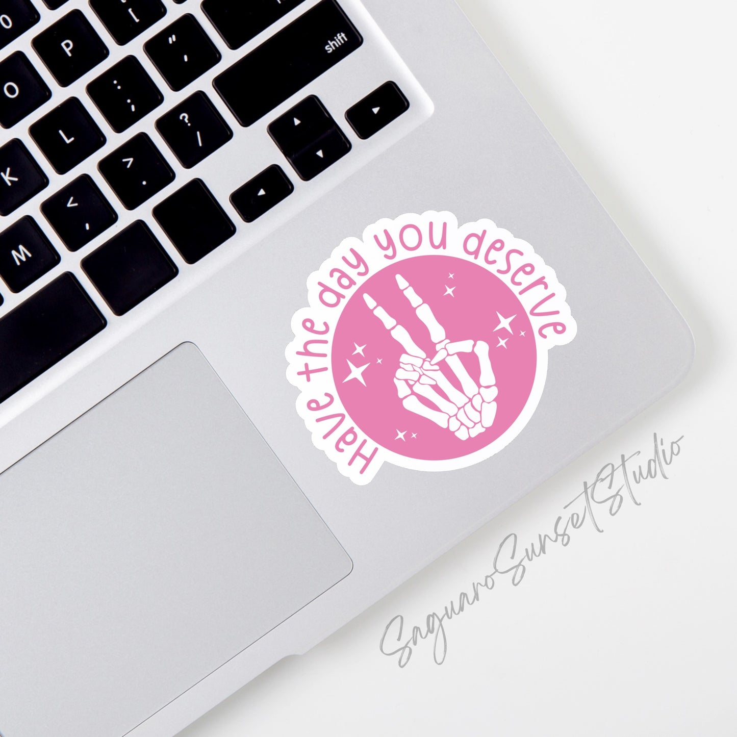 A vinyl sticker featuring a skeleton hand giving a peace sign with the phrase "Have the Day You Deserve" written around it