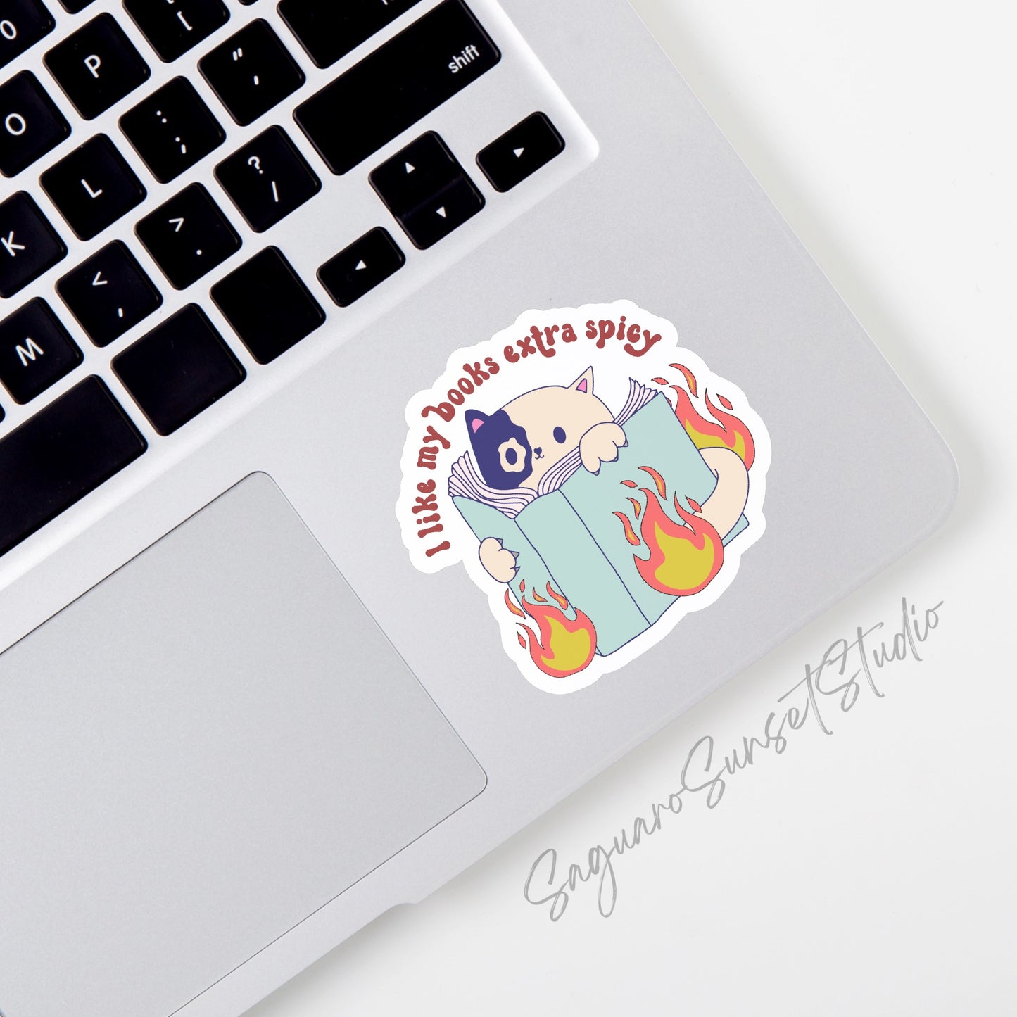 Sticker with the text "I Like My Books Extra Spicy" featuring a cute cat peeking over a book with playful flames. 