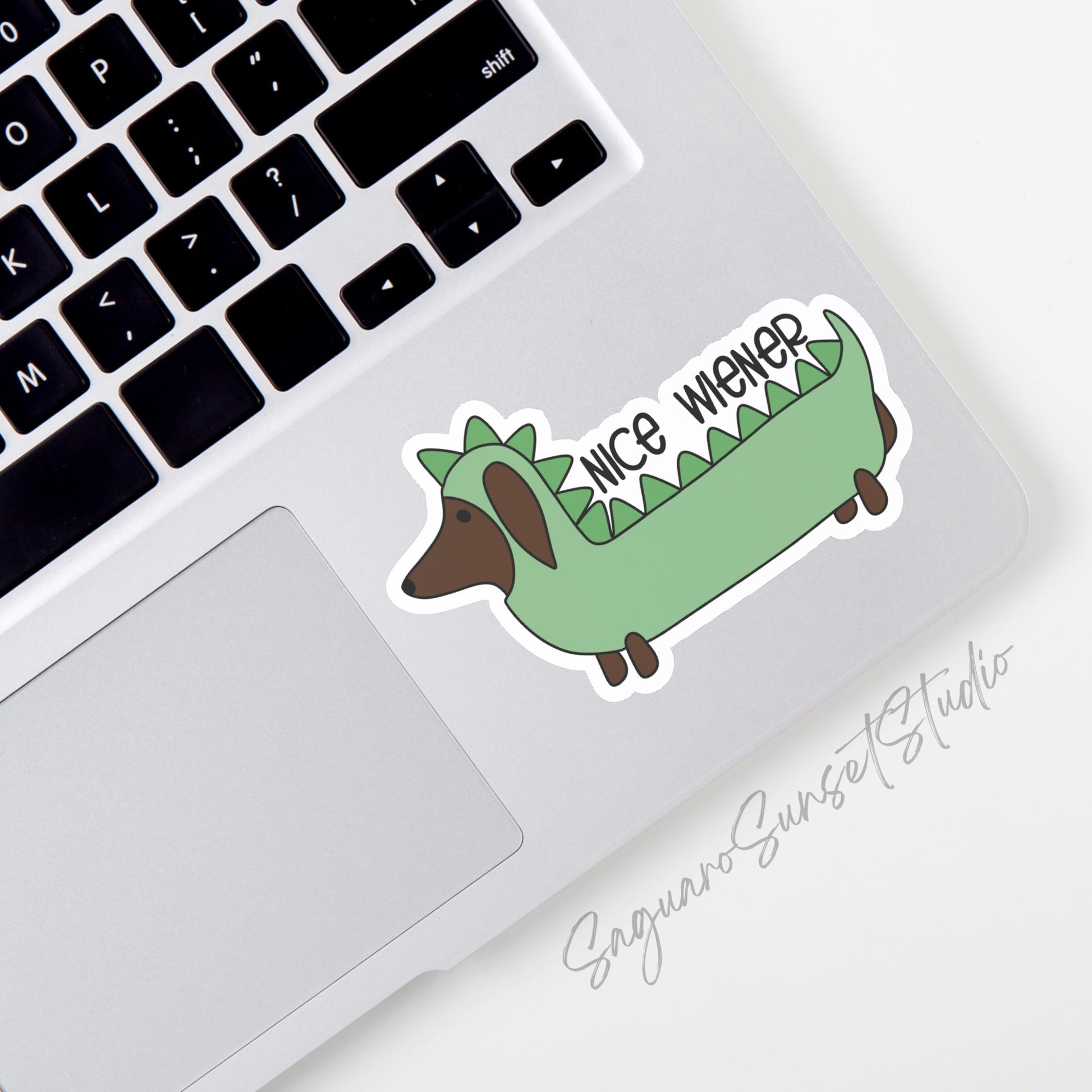 Sticker featuring a dachshund dressed in a green dinosaur costume with the phrase "Nice Wiener"