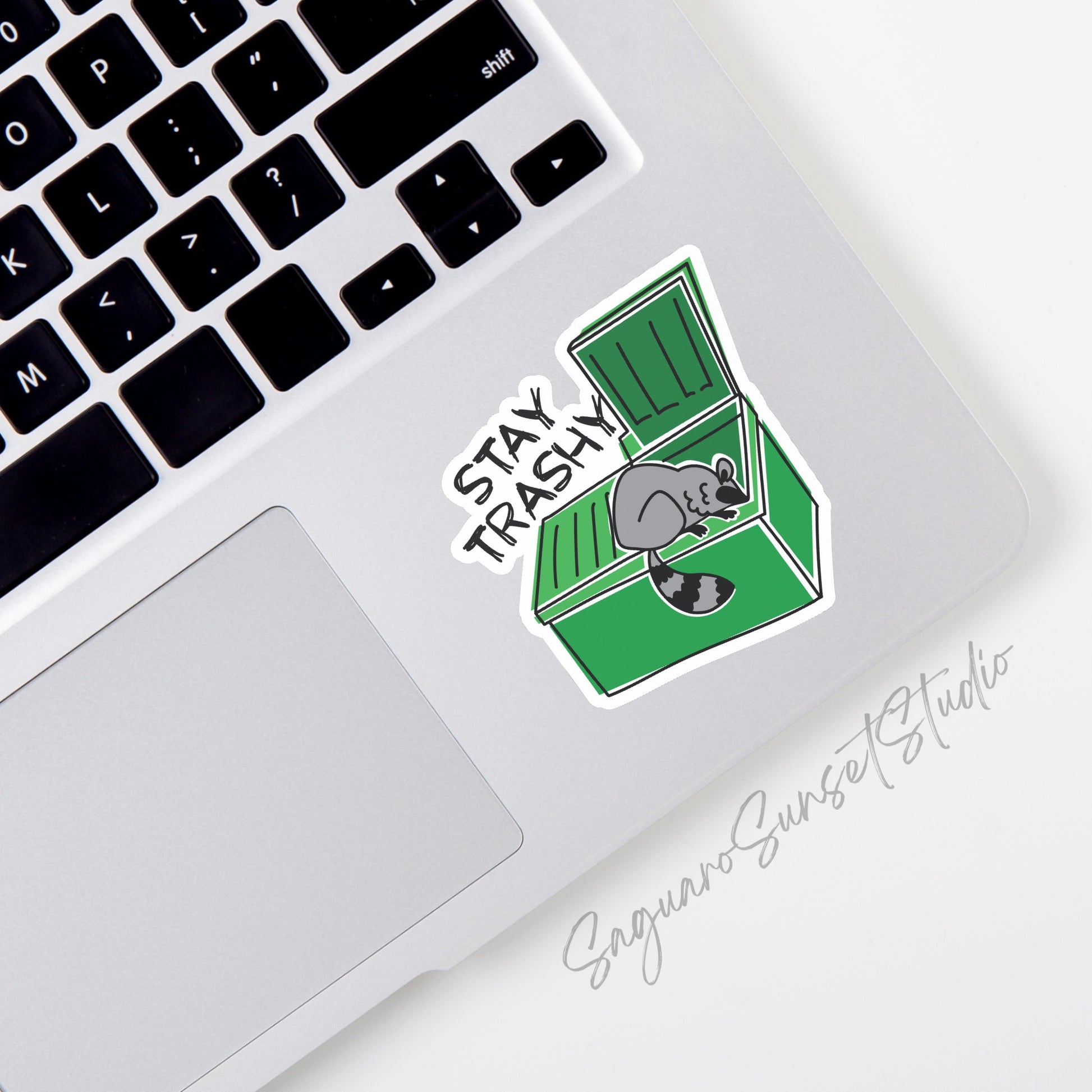 Sticker with the phrase "Stay Trashy" showing a raccoon (trash panda) in a dumpster, perfect for adding a touch of humor to your belongings.