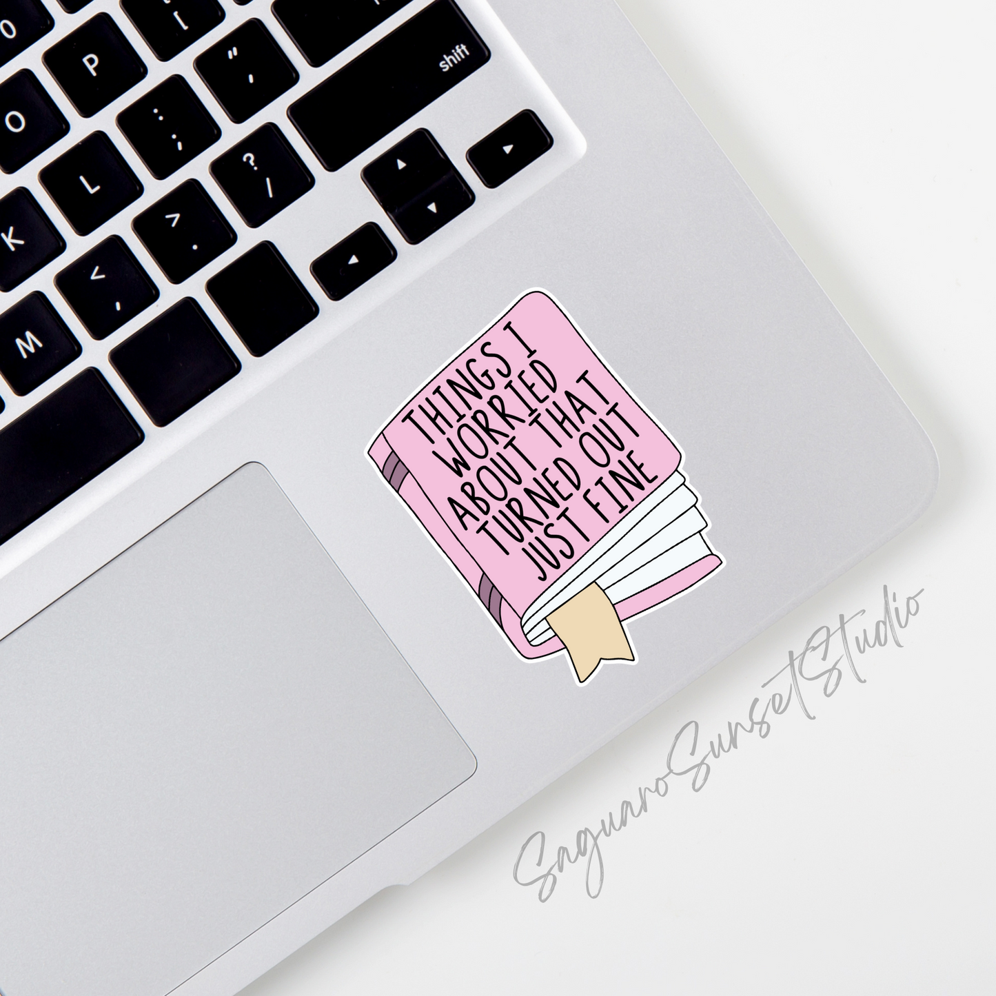 A sticker featuring a pink book with the text "Things I Worried About That Turned Out Just Fine" in bold black letters, complete with a beige bookmark sticking out.