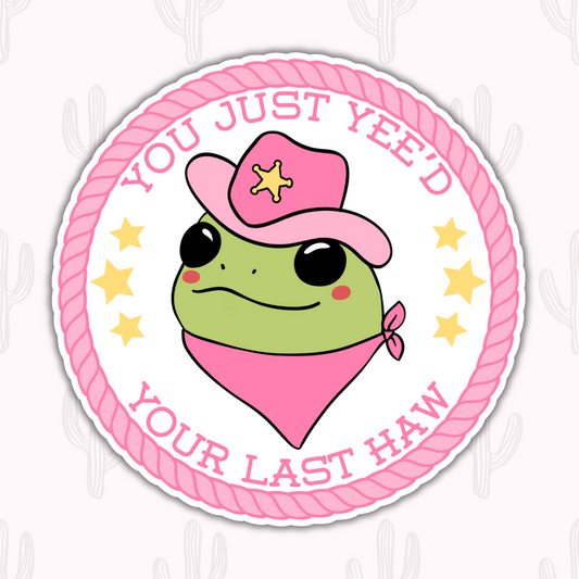 A round sticker featuring a green frog wearing a pink cowboy hat and bandana, surrounded by a pink rope border with the text "You Just Yee’d Your Last Haw" and yellow stars for added flair.