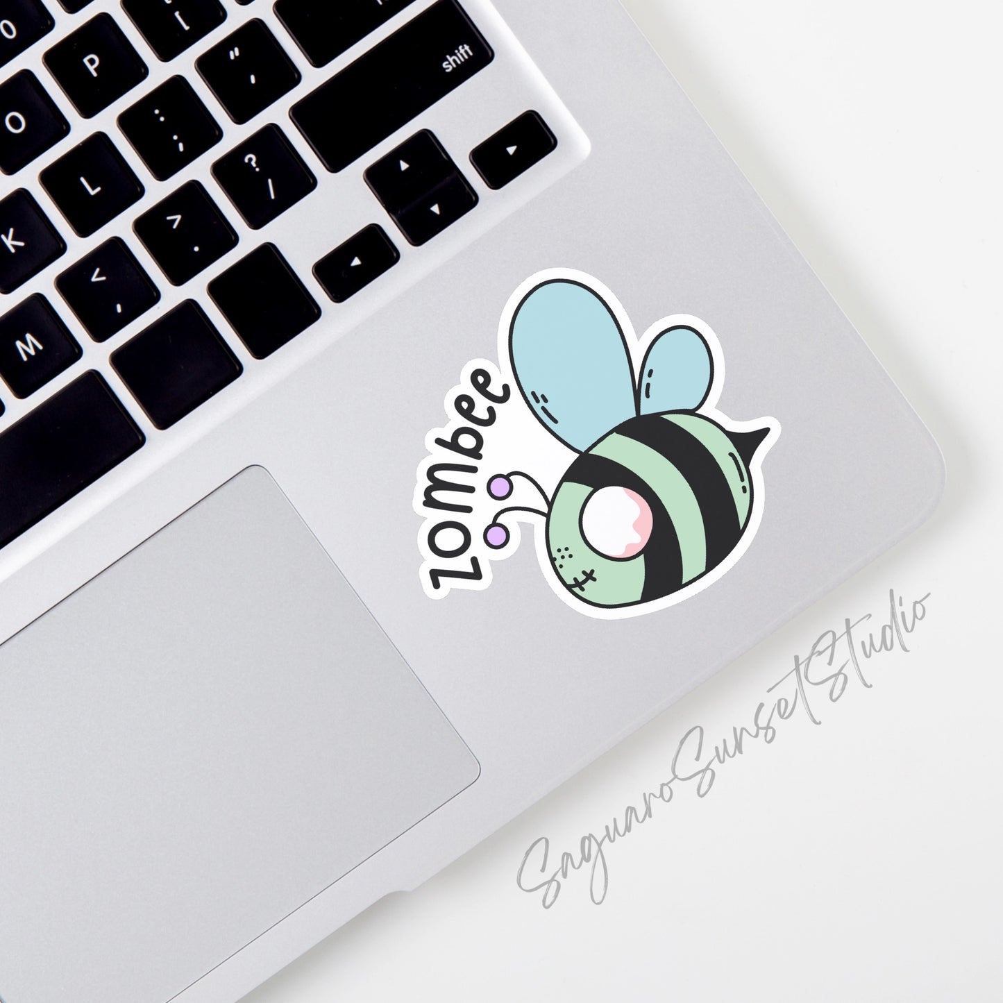 A sticker featuring a cartoon bee with a zombie twist, labeled "zombee" in black text. The bee has pastel blue wings, pink eyes, and green and black stripes, with playful, undead-themed details. 