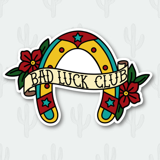 Upside down horseshoe sticker with red, yellow, and teal colors. Tan banner reads 'bad luck club' with red flowers on the sides.