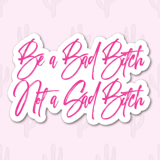 Sticker with pink cursive text 'be a bad bitch not a sad bitch' with a white outline around it.