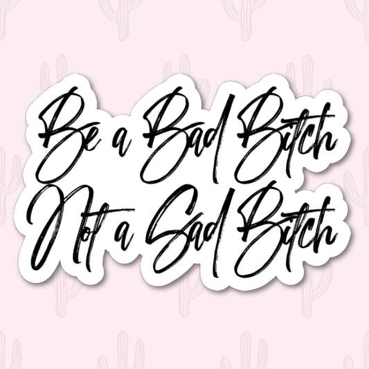 Sticker with black cursive text 'be a bad bitch not a sad bitch' with a white outline around it.