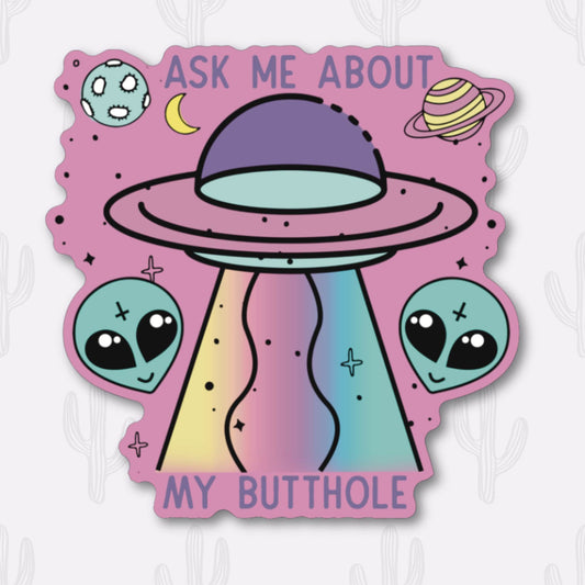 A sticker featuring the phrase "Ask Me About My Butthole" written in purple text above a whimsical UFO emitting rainbow beams. The design includes two friendly alien faces, planets, and stars against a pink background. 