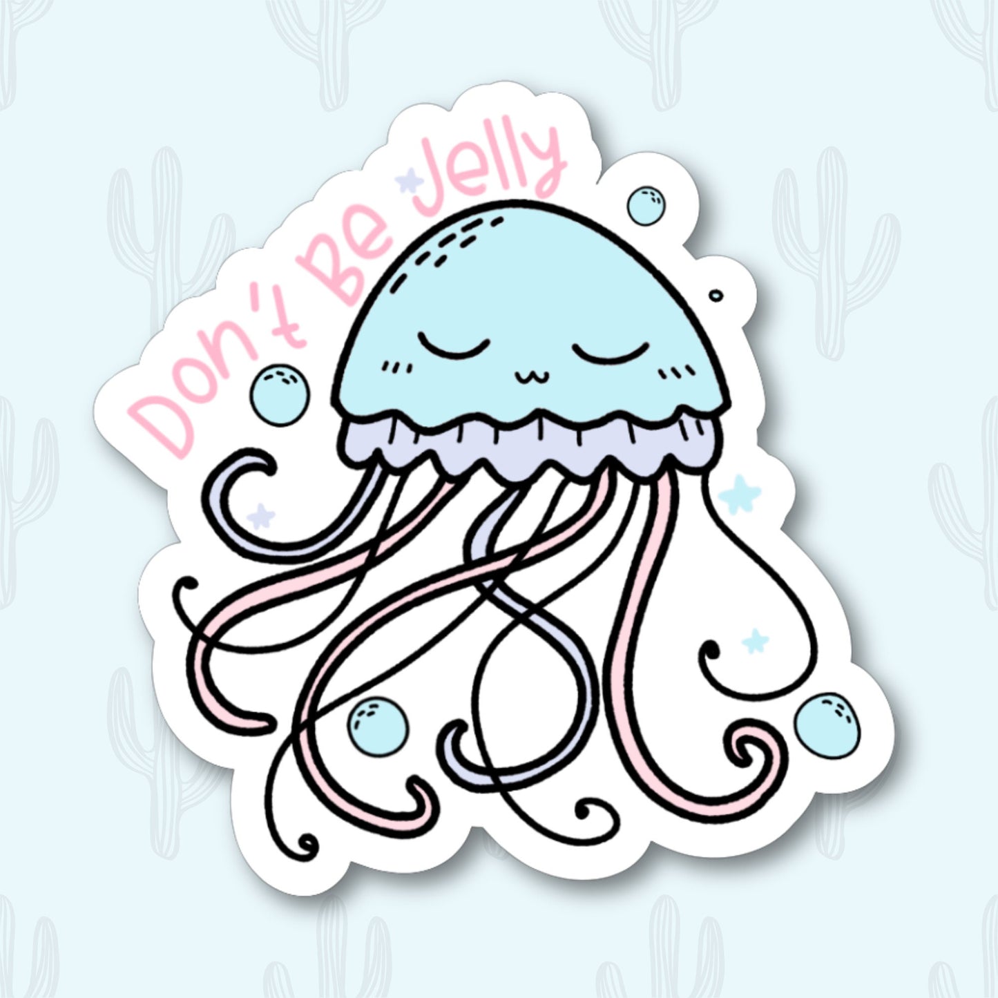 A vinyl sticker featuring a cute, pastel blue jellyfish with closed eyes and a peaceful expression. The jellyfish has flowing tentacles with pink accents and is surrounded by small bubbles and stars. The phrase "Don't Be Jelly" is written in pink text above the jellyfish.