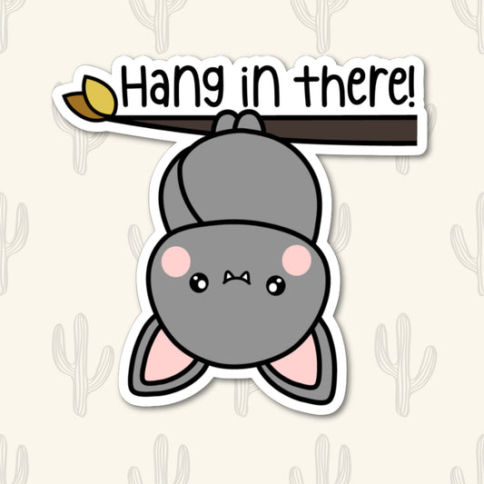 A vinyl sticker featuring a cute bat hanging upside down from a branch with the phrase "Hang in There!" written above