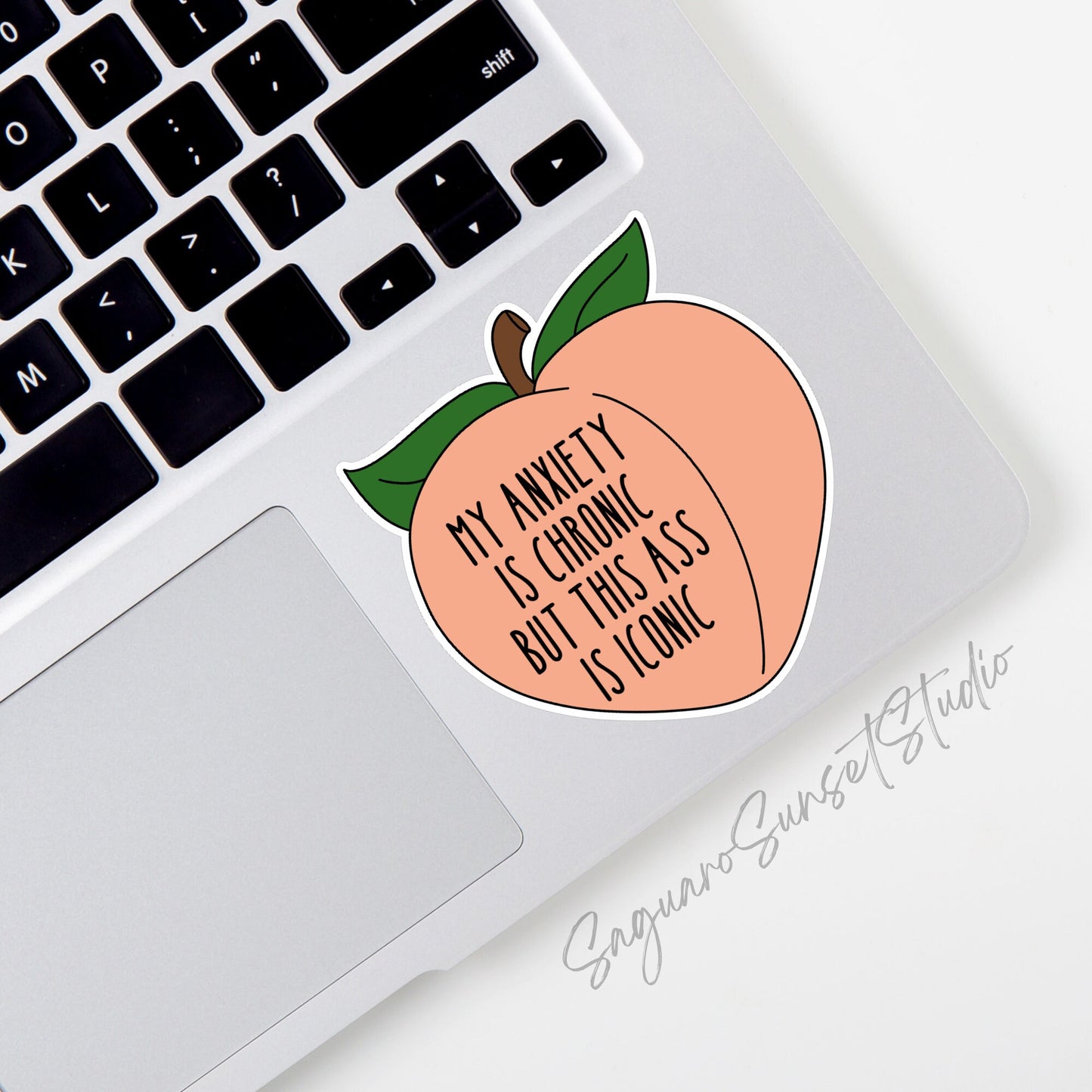 A sticker featuring the phrase "My anxiety is chronic but this ass is iconic" written in black text on a peach-shaped background with green leaves at the top. 