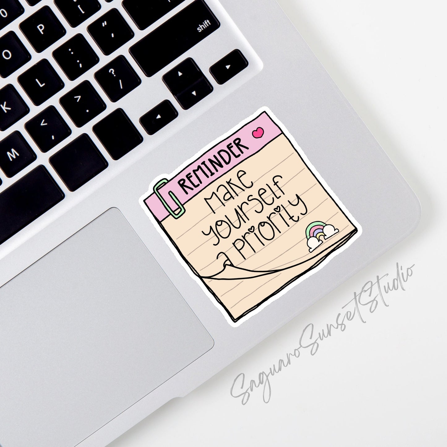 A sticker featuring a notepad with a pink header labeled "Reminder" and a heart icon, with the phrase "Make Yourself a Priority" written below. The design includes a cute paperclip and a small rainbow at the bottom. 