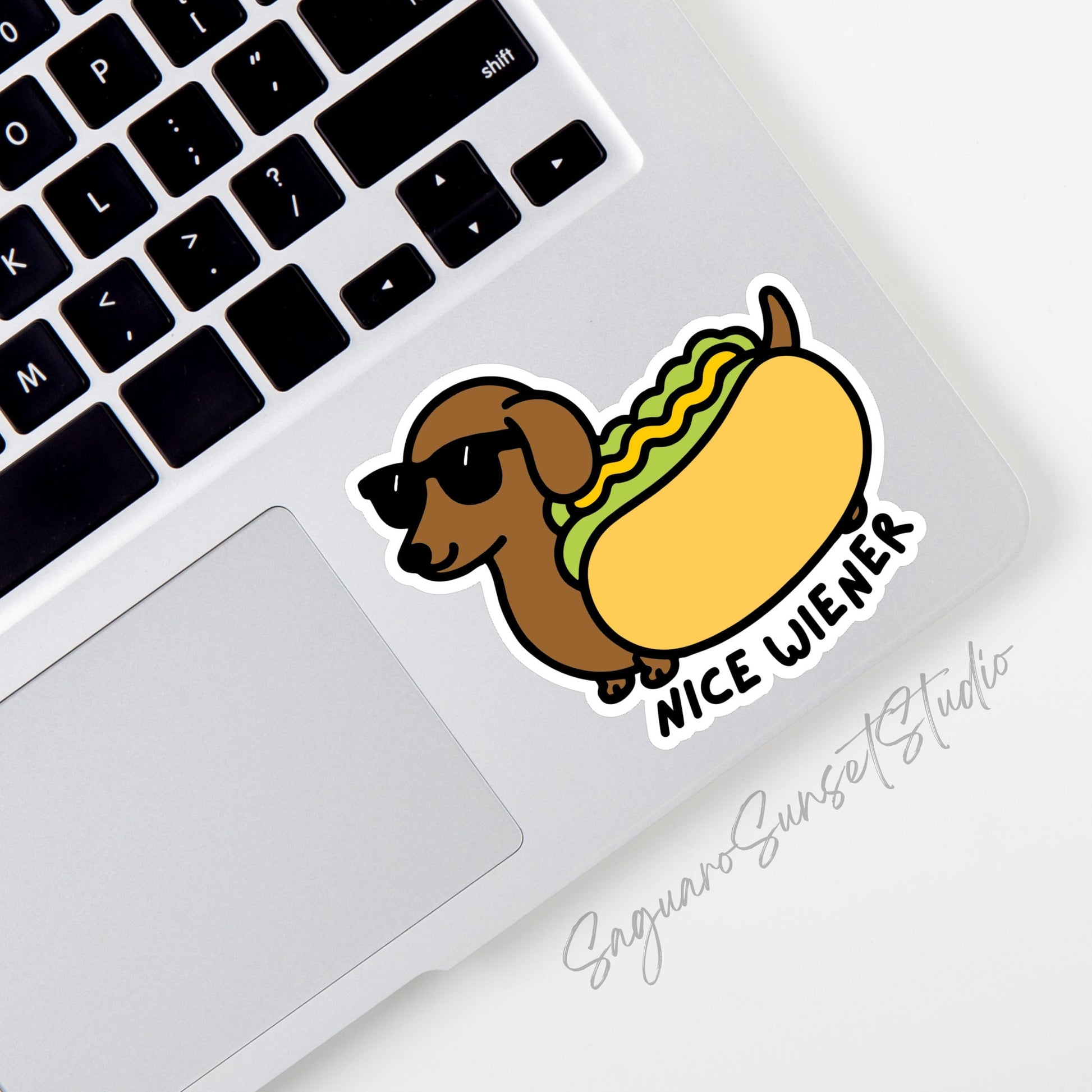 A sticker of a Dachshund wearing sunglasses and is dressed as a hot dog. The phrase under the sticker says 'Nice Wiener'